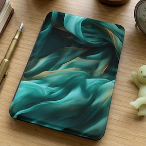 Puede incluir: Una funda rectangular, probablemente para una tableta o un lector electrónico, presenta un diseño abstracto en color turquesa y dorado. El patrón sugiere tela o agua fluyendo, con detalles en turquesa oscuro y dorado. La funda está sobre una superficie de madera.