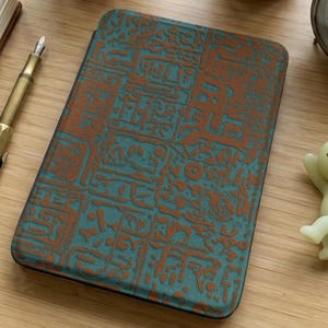 May include: A rectangular teal and brown tablet case with a textured, embossed design. The case features a repeating pattern of stylized symbols in a contrasting brown color. The case is likely made of leather or a similar material.