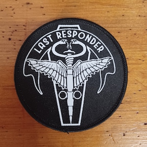 以下が含まれることがあります： 「Last Responder」というテキストと、翼のある医療シンボルのスタイリッシュな画像が刺繍された黒と白のパッチ