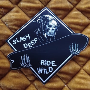 May include: Black and white sticker featuring a skeleton in a hooded robe holding a skateboard. The skateboard has the text "Ride Wild" and the text "Slash Deep" is on the sticker.