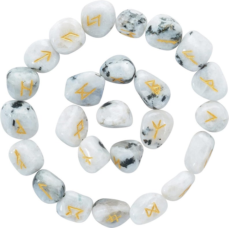May include: A collection of twenty-one white and gray rune stones arranged in a spiral. Each stone has a gold-colored rune symbol. The stones are smooth and polished, with a mix of white, gray, and black coloration.