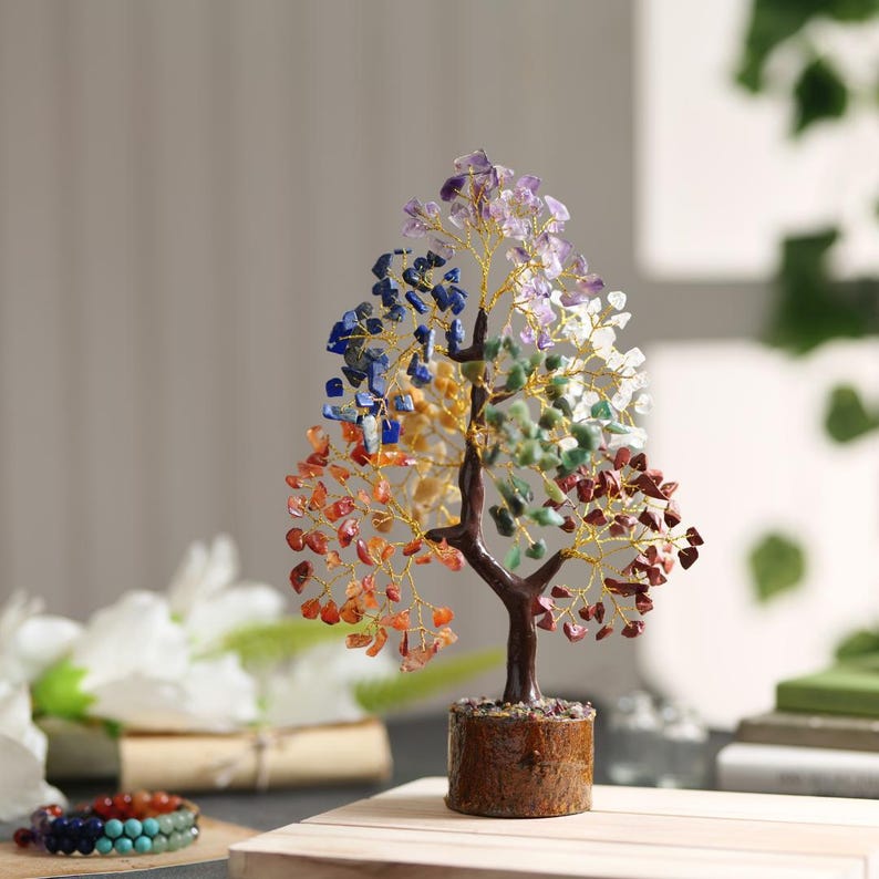 Peut inclure: Un arbre en cristal avec sept pierres pr&eacute;cieuses de couleurs diff&eacute;rentes, dont l'am&eacute;thyste, le lapis-lazuli, la citrine, la cornaline, l'aventurine verte, le jaspe rouge et le quartz clair. L'arbre est fait de fil et les pierres pr&eacute;cieuses sont attach&eacute;es au fil. L'arbre est pos&eacute; sur une base en bois.