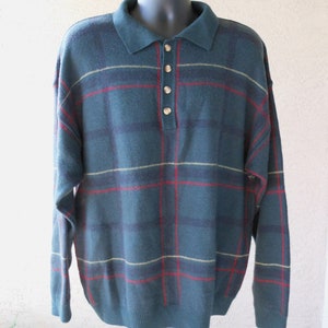 May include: A teal plaid sweater with a polo collar and three buttons. The sweater features a pattern of red and yellow lines over a dark teal background. The long-sleeved sweater is displayed on a black mannequin.