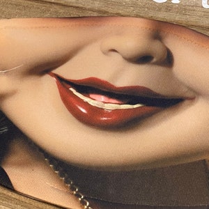 May include: A close-up of a face mask with a printed image of a woman's smiling mouth with red lipstick. The mask is made of a soft, brown fabric.