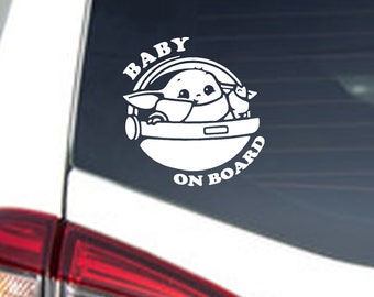 Op de afbeelding: Witte auto sticker voor het raam met een cartoon afbeelding van een baby Yoda-personage in een ruimteschip met de tekst "Baby On Board".