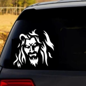 May include: White vinyl decal of a stylized face with long hair, resembling a rock musician, on a black car window.