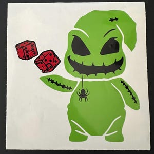 May include: Green cartoon character with a stitched-up body and a spider hanging from its neck. The character is holding two red dice in its hands.