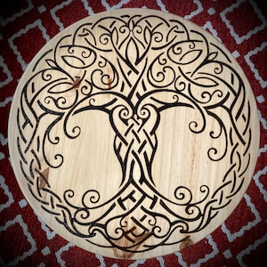 May include: A circular wooden board with a black tree of life design burned into the surface. The tree has intricate branches and swirls.