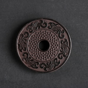 Peut inclure: Un dessous de tasse en céramique brun foncé avec un motif décoratif d'oiseaux et de nuages stylisés. Le dessous de tasse a un trou central pour drainer l'eau.