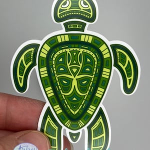 Op de afbeelding: Groene en gele gepatroneerde schildpad sticker met een witte omtrek. De schildpad heeft een geometrisch ontwerp met een gestileerd hoofd en schild.