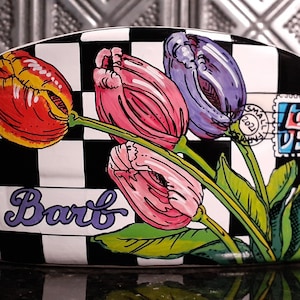 May include: A white ceramic bread box with a black and white checkered pattern. The box is decorated with a colorful floral design featuring tulips in shades of pink, purple, red, and yellow. The word "Barb" is written in purple cursive on the front of the box.