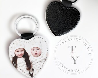 May include: Two heart-shaped leather keychains with silver key rings. One keychain is black and the other is white with a photo of two children. The white keychain has the text "Keep Sakes Treasure To You T Y" printed on it.