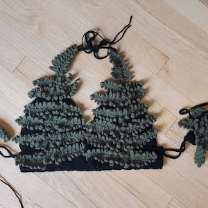 May include: A green and black crocheted halter top with a tree design. The top has two matching detachable pieces that can be worn as arm warmers or wrist cuffs.
