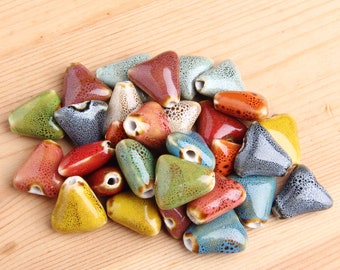 May include: A collection of colorful ceramic triangle beads with speckled and glazed finishes. The beads are arranged in a pile on a wooden surface.