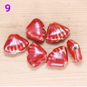 May include: Six red ceramic beads in the shape of a heart with a white glaze. The beads have a textured surface and are perfect for jewelry making.