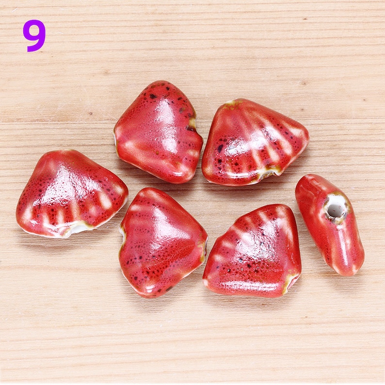 May include: Six red ceramic beads in the shape of a heart with a white glaze. The beads have a textured surface and are perfect for jewelry making.