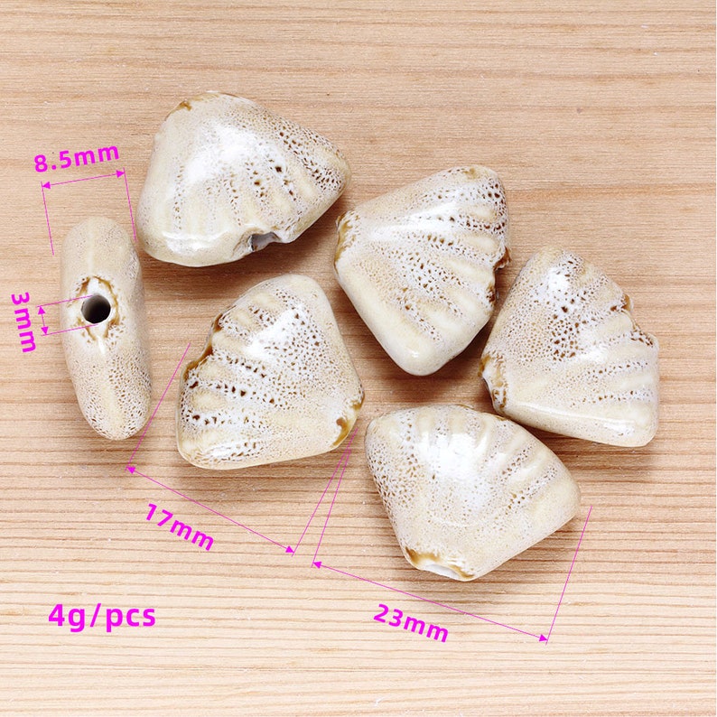 May include: Six ceramic beads in a light brown color with white speckles. The beads are shaped like a triangle with rounded edges. The beads are 23 mm wide and 17 mm tall. The beads are 4 grams per piece.