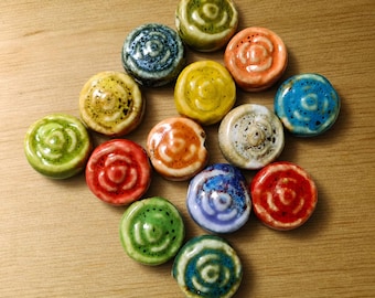 May include: A collection of colorful ceramic knobs in various shades of green, yellow, orange, red, blue, and white. Each knob features a spiral design and a glossy finish, arranged on a light brown wooden surface.