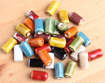 May include: A collection of colorful ceramic beads in various shapes and sizes. The beads are arranged in a pile on a wooden surface.