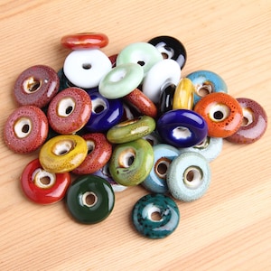 May include: Assortment of colorful ceramic donut-shaped beads with a hole in the center. The beads are in various shades of blue, green, red, yellow, and white.