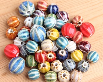 May include: A collection of colorful ceramic beads with various patterns and designs. The beads are a mix of blue, green, red, yellow, and white.