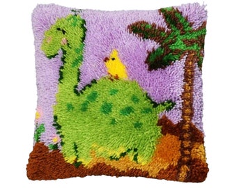May include: A purple and green plush pillow with a dinosaur and a yellow bird on it. The dinosaur is green with brown spots and the bird is yellow with a black beak. The pillow is surrounded by brown and green grass.