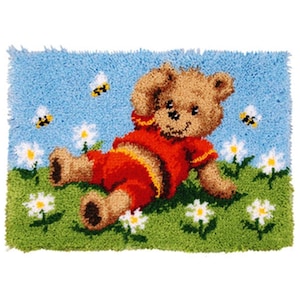 Puede incluir: Una alfombra de peluche con un oso de peluche marrón que lleva una camisa roja y está tumbado en un campo verde con margaritas blancas y abejas amarillas.