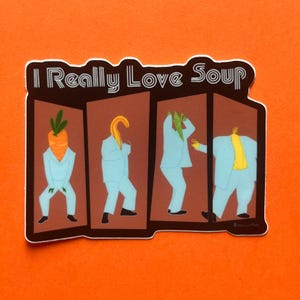 May include: A sticker with the text "I Really Love Soup" above four figures. Each figure is wearing a light blue suit and has a different vegetable for a head: a carrot, a yellow squash, green beans, and a yellow shirt.