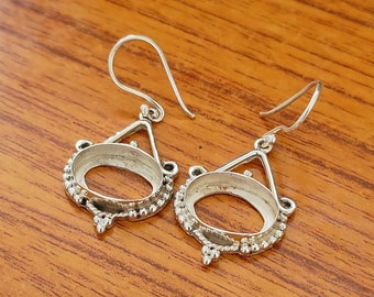 Può includere: Un paio di orecchini d'argento con una montatura ovale. Gli orecchini hanno un design delicato e decorato con piccole perline attorno al bordo della montatura.