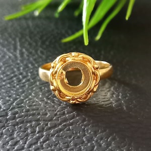 May include: A gold-toned ring with a round bezel setting. The bezel is decorated with a detailed design of small beads and a rope-like pattern.