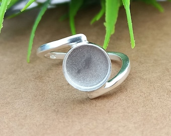 Könnte beinhalten: Silberring mit einer runden Fassung für einen Cabochon-Stein. Der Ring ist mit einem gebogenen Band gestaltet.