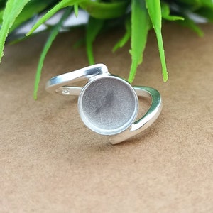 May include: Silver ring with a round bezel setting for a cabochon stone. The ring is designed with a curved band.
