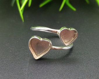 Può includere: Anello d'argento con due montature a forma di cuore. L'anello è progettato per essere indossato al dito, con i cuori rivolti verso l'alto.