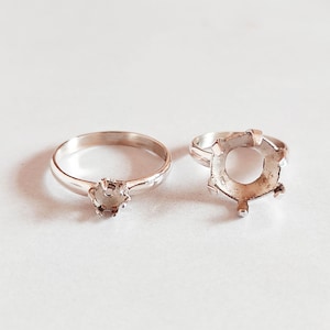 Puede incluir: Dos anillos de plata, uno con un engaste redondo y el otro con una banda lisa.