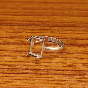 May include: A silver ring with a square-shaped setting for a gemstone. The ring is designed for a rectangular or square-shaped stone.