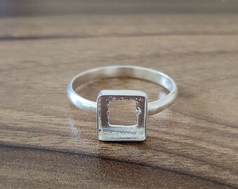 Op de afbeelding: Een zilveren ring met een vierkante uitsparing in het midden.