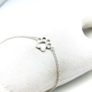 May include: A silver chain bracelet with a paw print charm. The charm is hollow and has a detailed design.