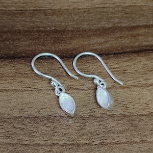 May include: A pair of silver dangle earrings featuring a white oval-shaped gemstone. The earrings have a simple design and are ideal for everyday wear.