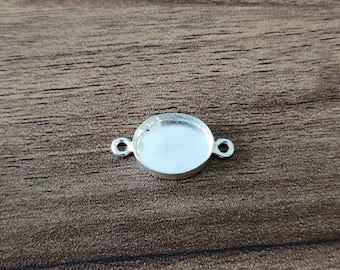 May include: Silver oval pendant tray with two jump rings for attaching to a necklace or bracelet. The tray is designed to hold a small cabochon or other decorative element.