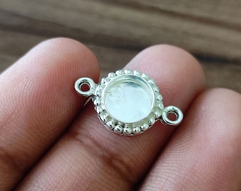 May include: Silver-toned pendant with a round bezel and two jump rings. The bezel has a beaded edge.