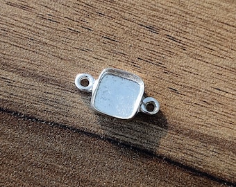 May include: Silver-toned metal connector with a square bezel for a gemstone or cabochon. The connector has two loops for attaching to a chain or other jewelry.
