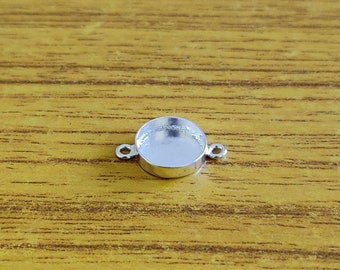 May include: Silver-toned round pendant with two loops on the side. The pendant has a smooth, shiny surface.