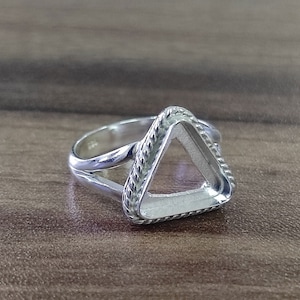 May include: A silver ring with a triangular shaped bezel. The bezel has a rope-like design around the edge.