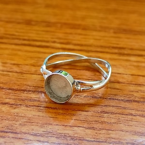 May include: A silver ring with a round, clear, glass-like setting. The ring has a twisted band design.