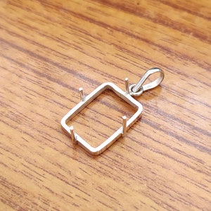 May include: Silver pendant setting with four prongs and a loop for attaching a chain. The setting is designed to hold a rectangular gemstone.