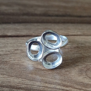 Könnte beinhalten: Ein silberner Ring mit drei ovalen Ausschnitten. Der Ring ist so konzipiert, dass er drei Steine oder Anhänger aufnehmen kann.