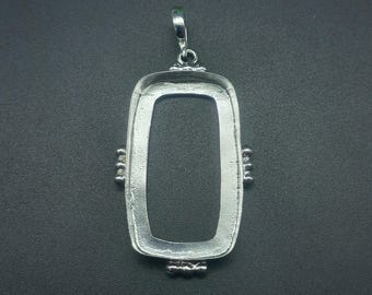 Puede incluir: Un colgante rectangular plateado con un lazo para una cadena. El colgante tiene un centro hueco y detalles decorativos en los lados y la parte inferior. El colgante está diseñado para sostener una piedra u otro inserto.