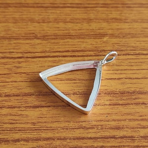 Puede incluir: Pendiente de plata de forma triangular con un bucle en la parte superior para sujetar una cadena. El pendiente es hueco y tiene un acabado liso y pulido.