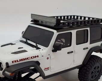 May include: White Jeep Wrangler Rubicon with a black roof rack and a light bar. The Jeep has black wheels and tires and a red "Rubicon" decal on the side.