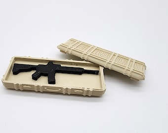 Puede incluir: Una caja de plástico beige con una silueta moldeada de un rifle en su interior. La caja está abierta y la tapa está apoyada junto a ella.